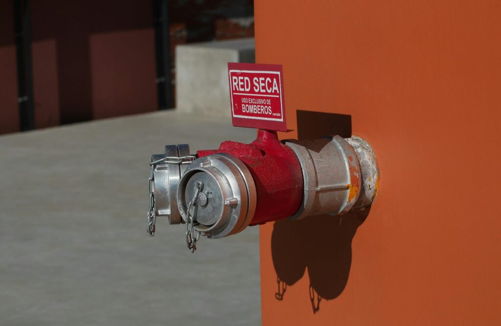 Close-up of a red hydrant with shadow on an orange wall, featuring a Spanish sign.
