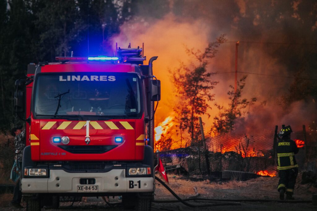 Intense forest fire scene with firefighters and bright red firetruck in action.