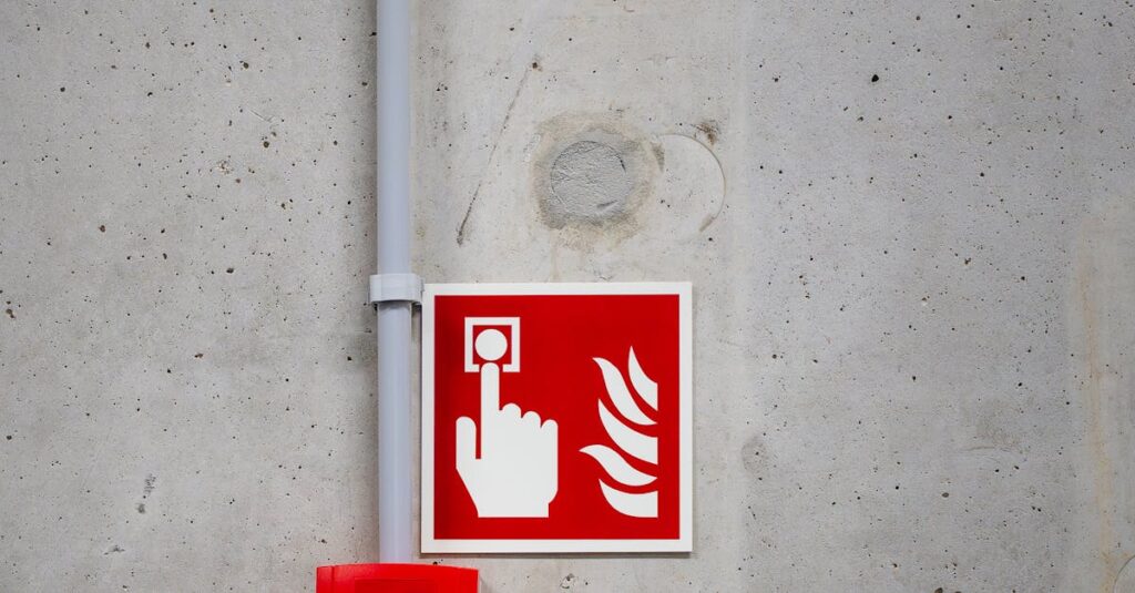 A red fire alarm switch with a warning sign on a concrete wall, highlighting safety in industrial settings.